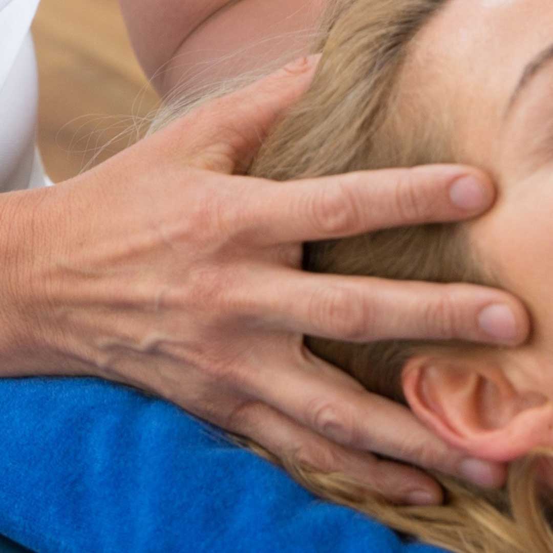 Erwachsene Frau, die auf dem Rücken liegt, wird am Kopf von zwei Händen berührt während der Behandlung
